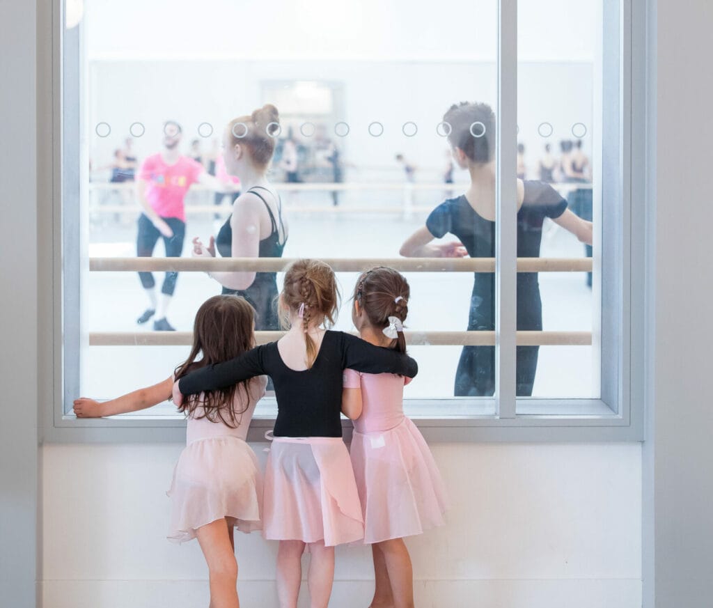 Image of three young children looking through window into older dance for inspiration