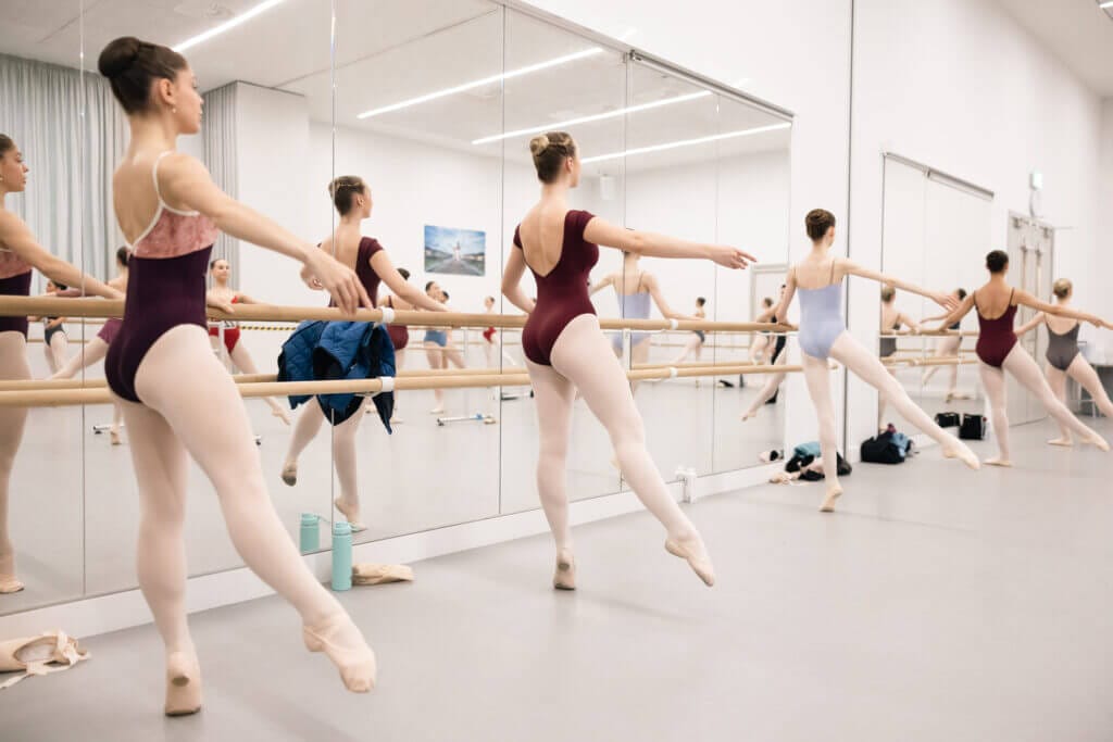 Image showing candidates in warm up at the barre Female dancers in tights leotards and ballet shoes with hair in a bun rise up on a demi with leg a la seconde