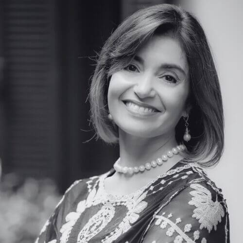 Portrait of a smiling woman wearing a pearl necklace and floral patterned blouse looking at the camera