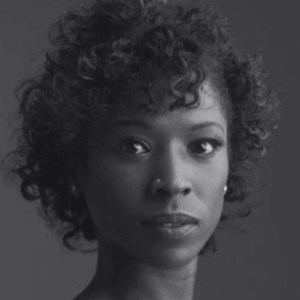 Close up grayscale portrait of a woman with short curly hair facing forward and looking at the camera
