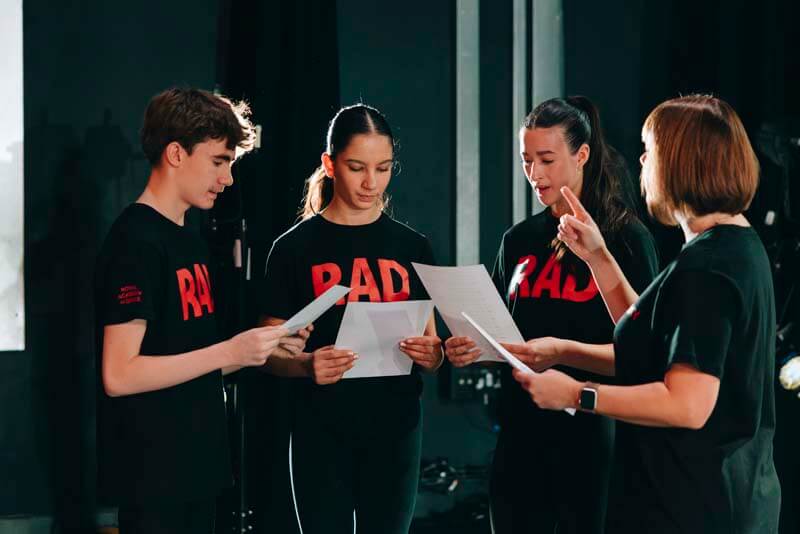 Four performers in black RAD shirts read scripts in a rehearsal studio