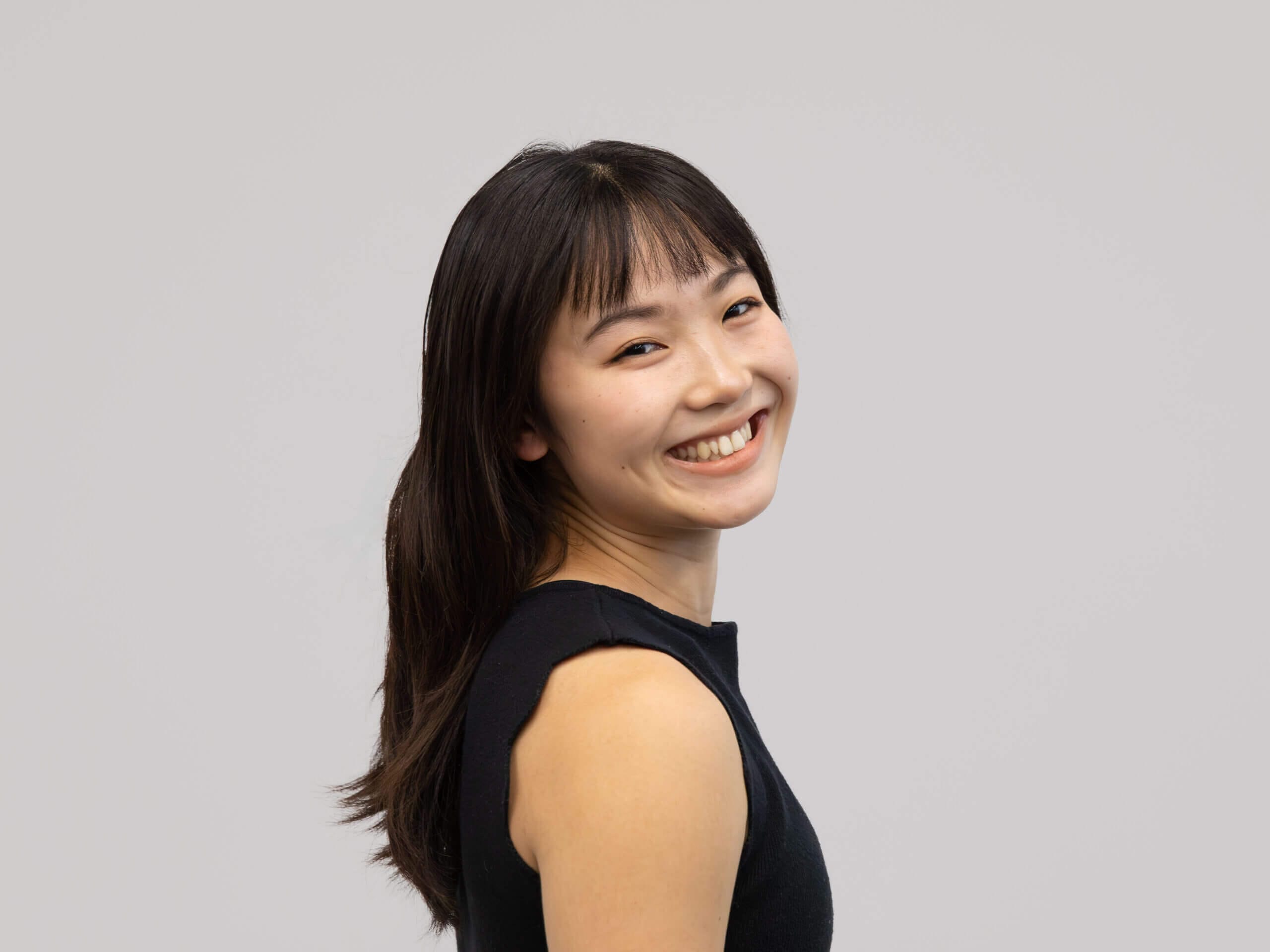 Smiling woman with long dark hair photographed in a studio turned slightly to the side against a gray background