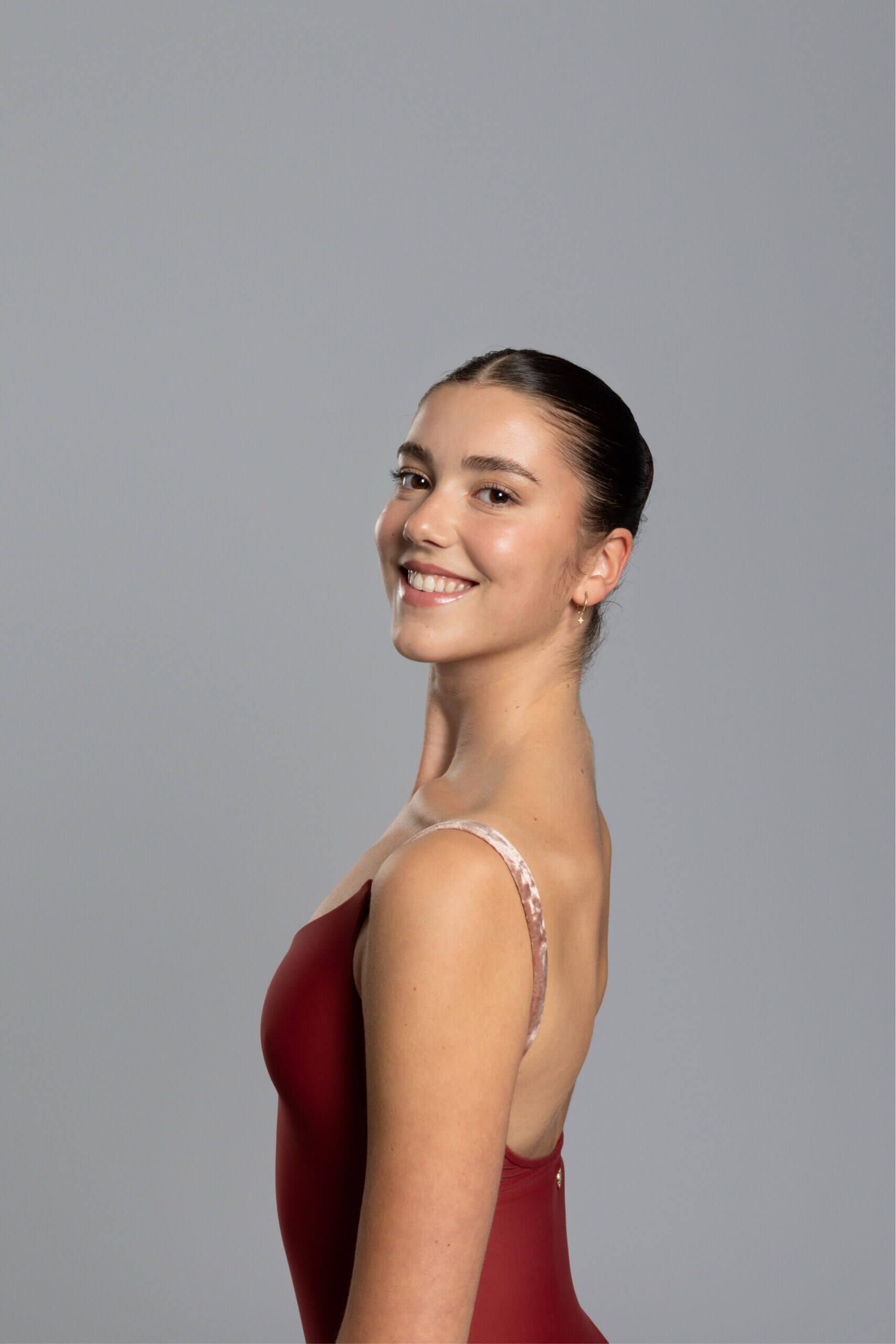 Smiling woman in a red dress posed in profile against a gray studio background