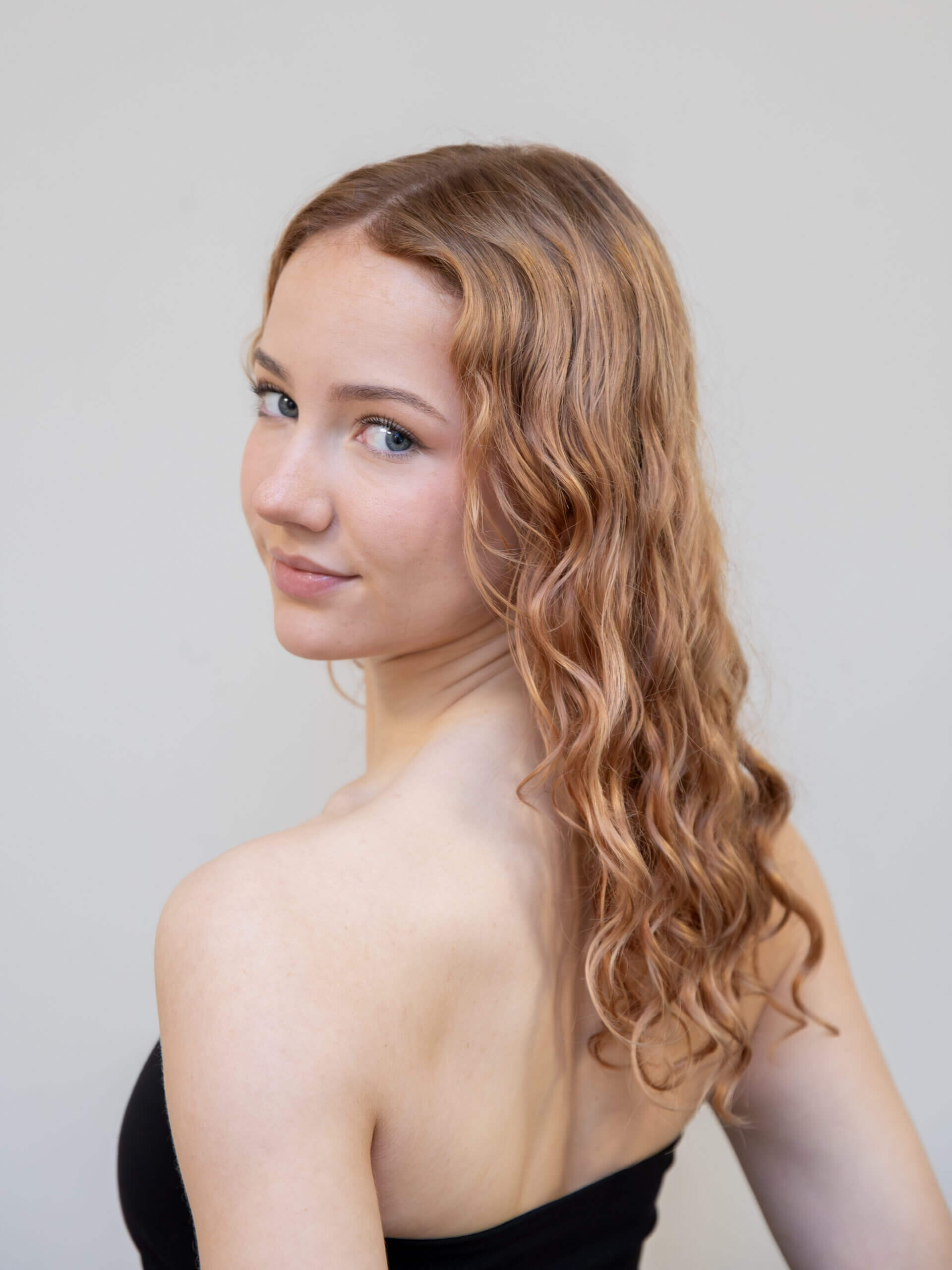 Portrait of a woman with wavy red hair wearing a black top looking over her shoulder toward the camera