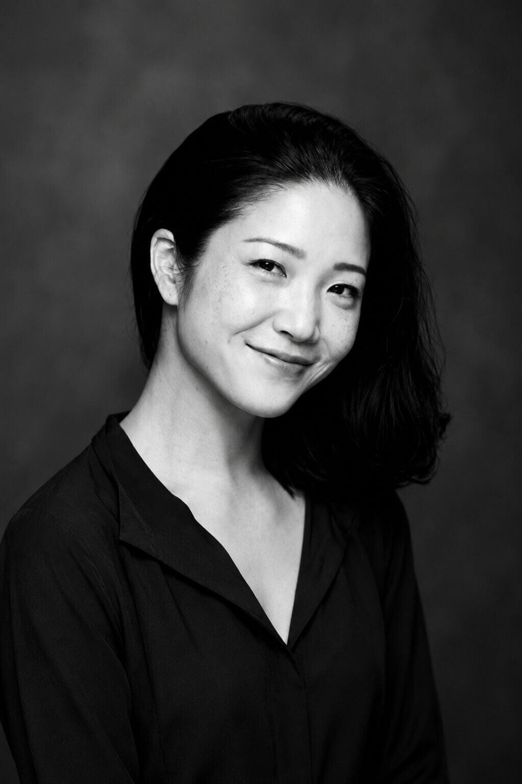 Black and white portrait of a smiling woman with dark hair wearing a black blouse in a studio setting